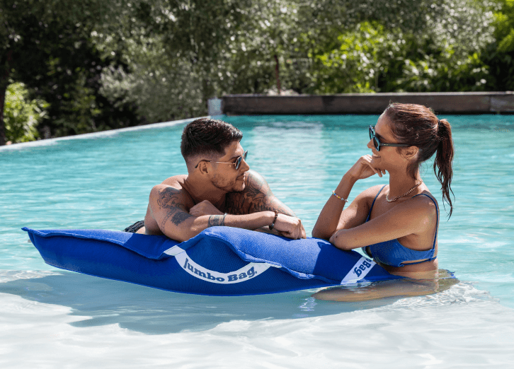 un jeune couple discute dans sa piscine en se reposant sur un coussin flottant bleu